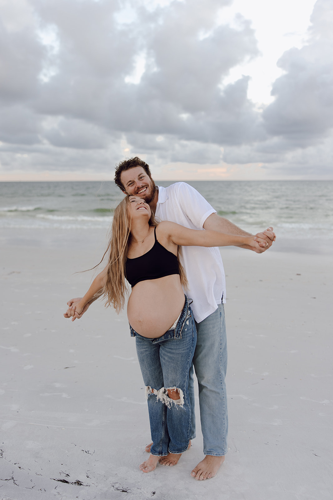 the couple doing the airplane pose on the beach for their couple photo maternity session