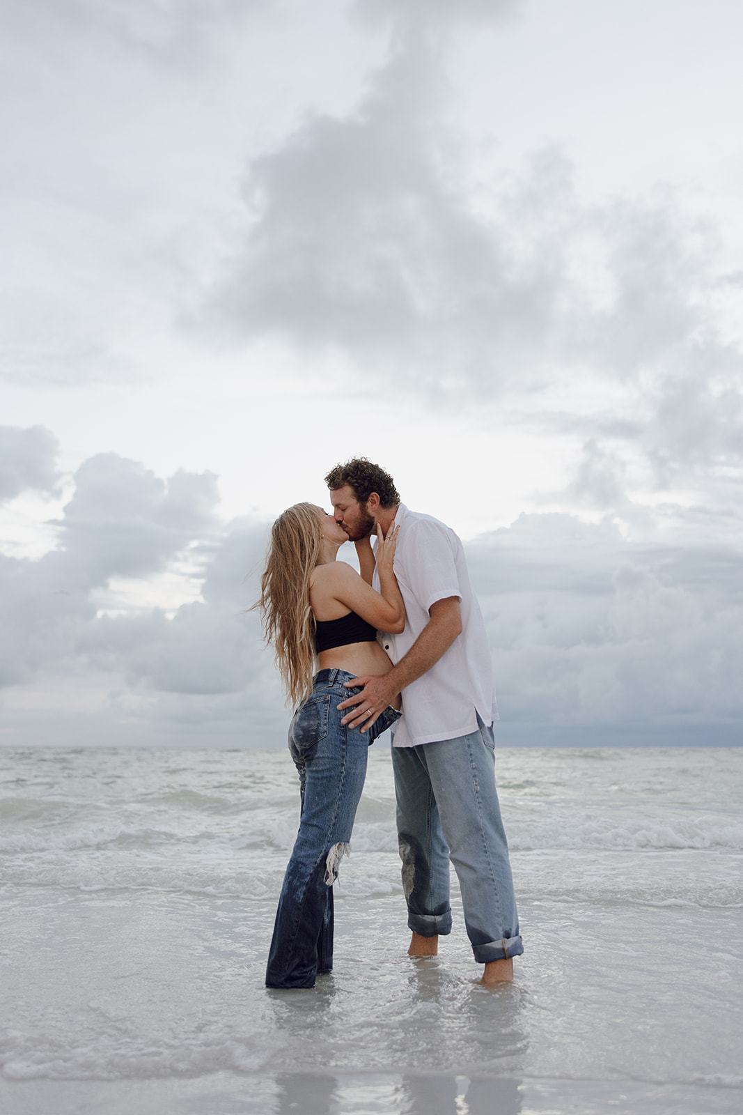 the couple kissing in the water with the storm clouds overhead