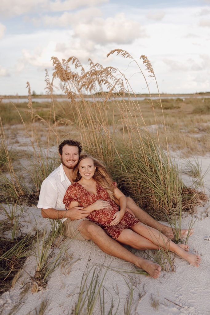 the couple sitting in the sand in the grasses on the beach while on the beach