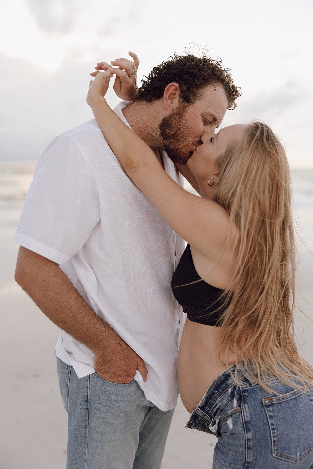 the couple kissing on the beach during their couple photo maternity session