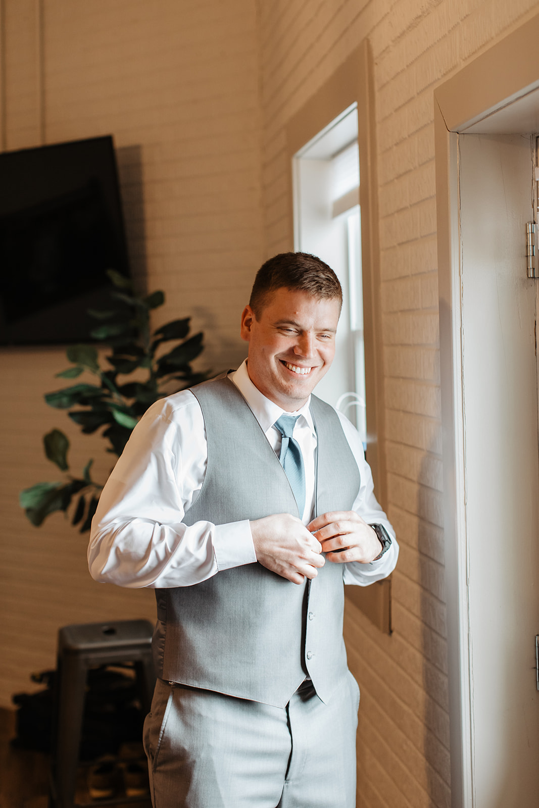 the groom putting on his vest and smiling at the camera