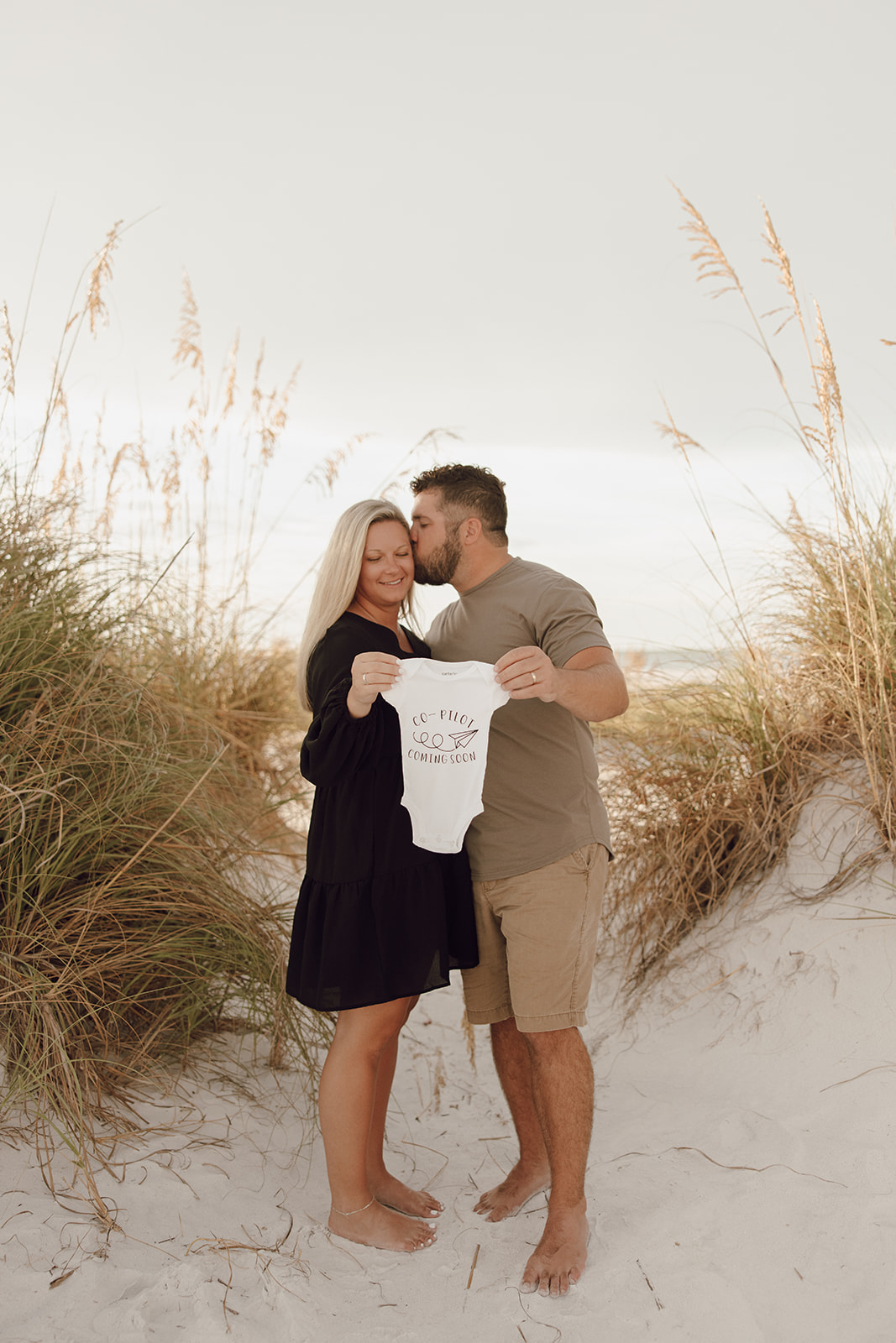 the couple holding a baby onesie as an idea for beach photoshoot