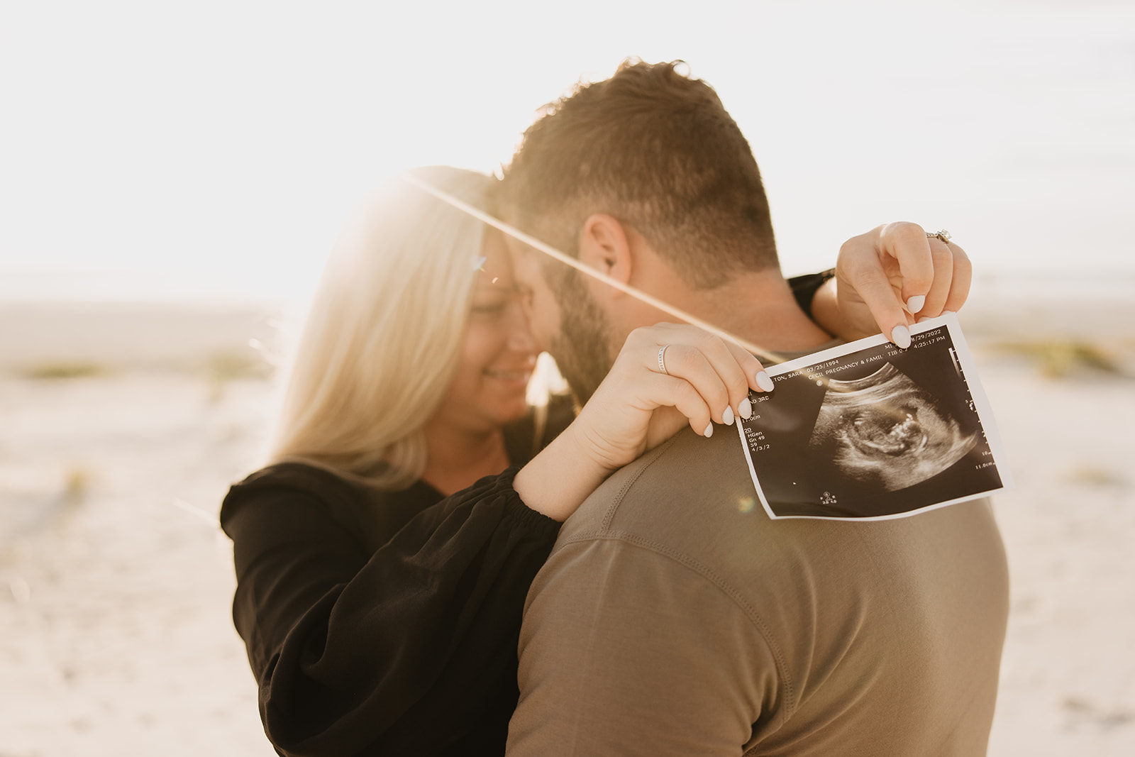 the wife wrapping her arms around the neck of her husband with the baby ultrasound photo
