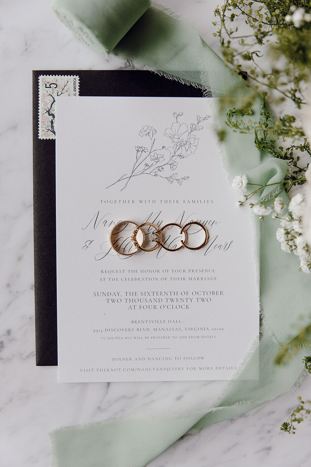 the wedding details with the wedding rings on top of the wedding invitations