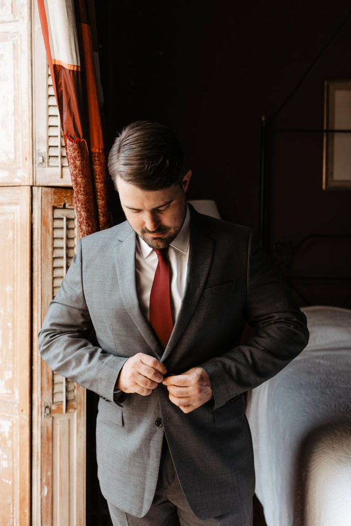 the groom putting on his suit jacket for his hotel wedding