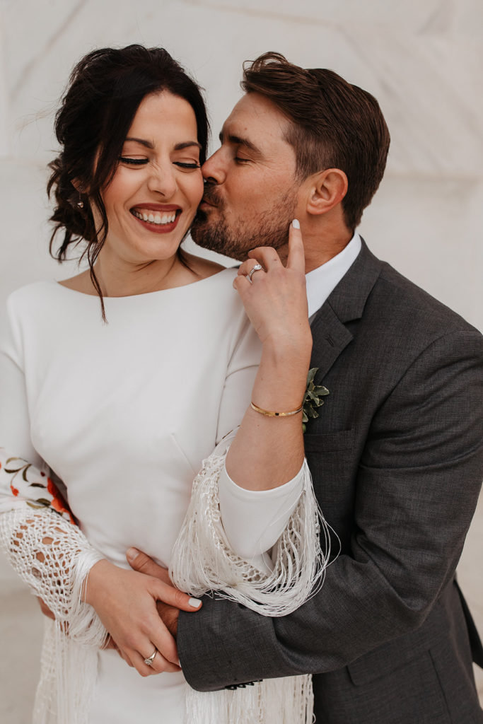 the couple laughing together as the groom kisses the bride's cheek 