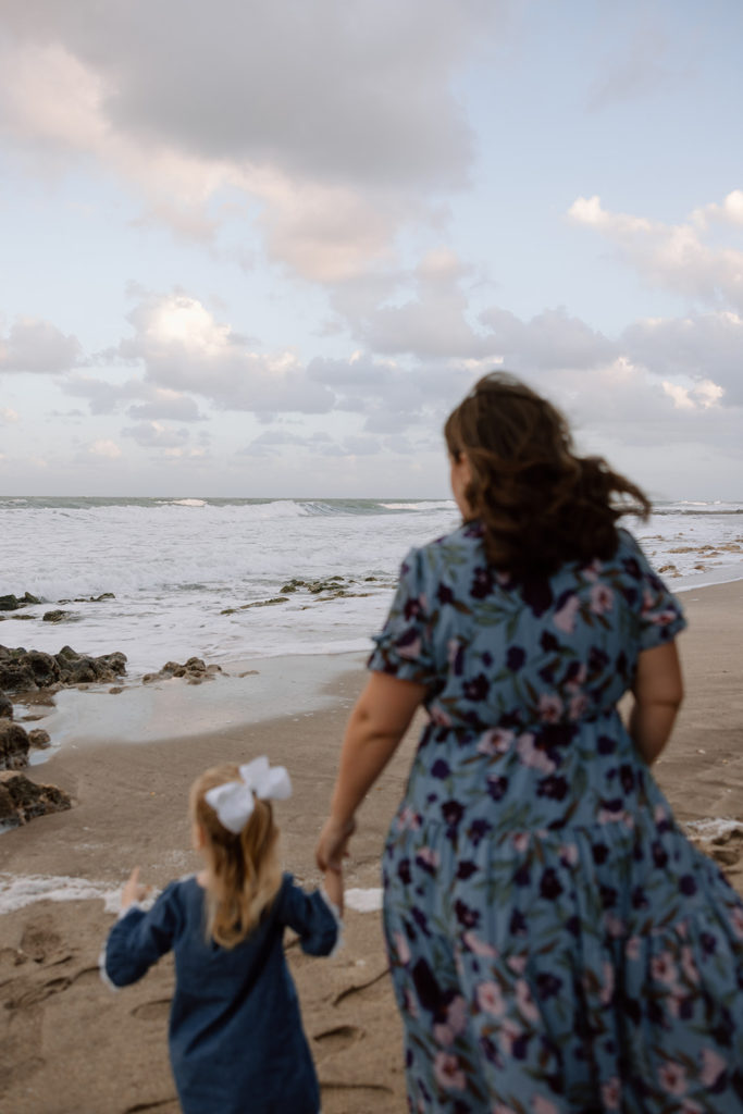 the mom and daughter holding hands as the walk down the beach during family photos