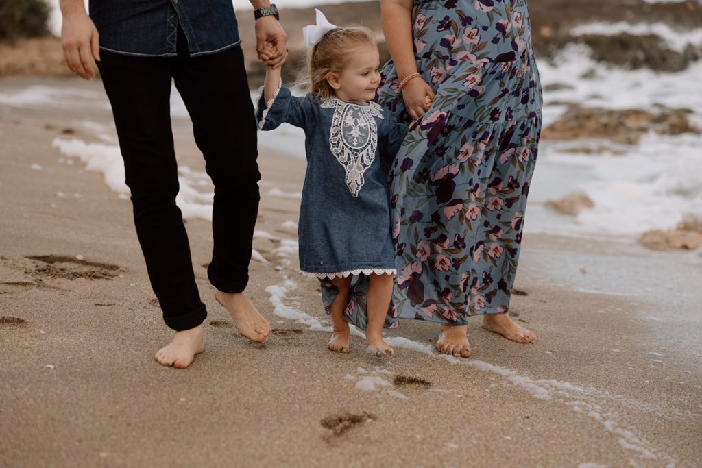 the couple holding the little girl's hands for the beach family photography