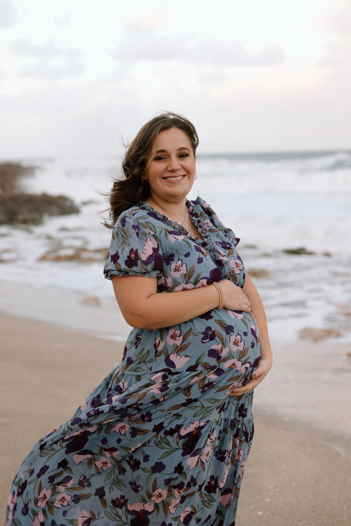 the mom standing on the beach with her baby bump