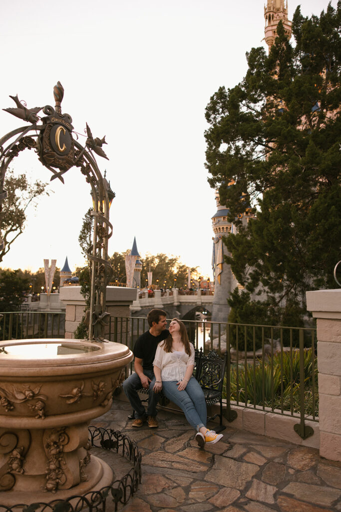 the couple sitting on a bench in the Magic Kingdom for engagement photos