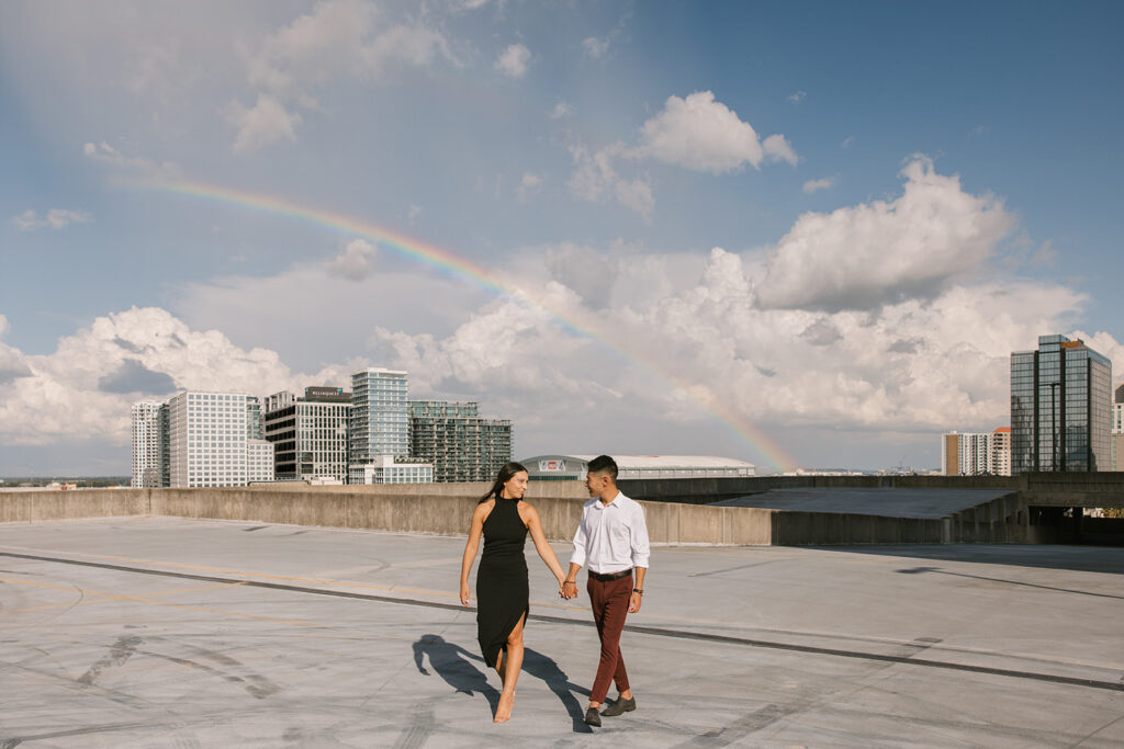 the engaged couple walking on the rooftop downtown Tampa with a rainbow in the background