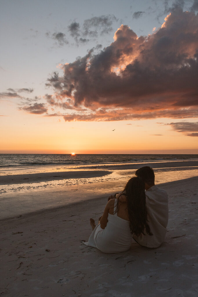 the engaged couple sitting on the beach together during their engagement photos