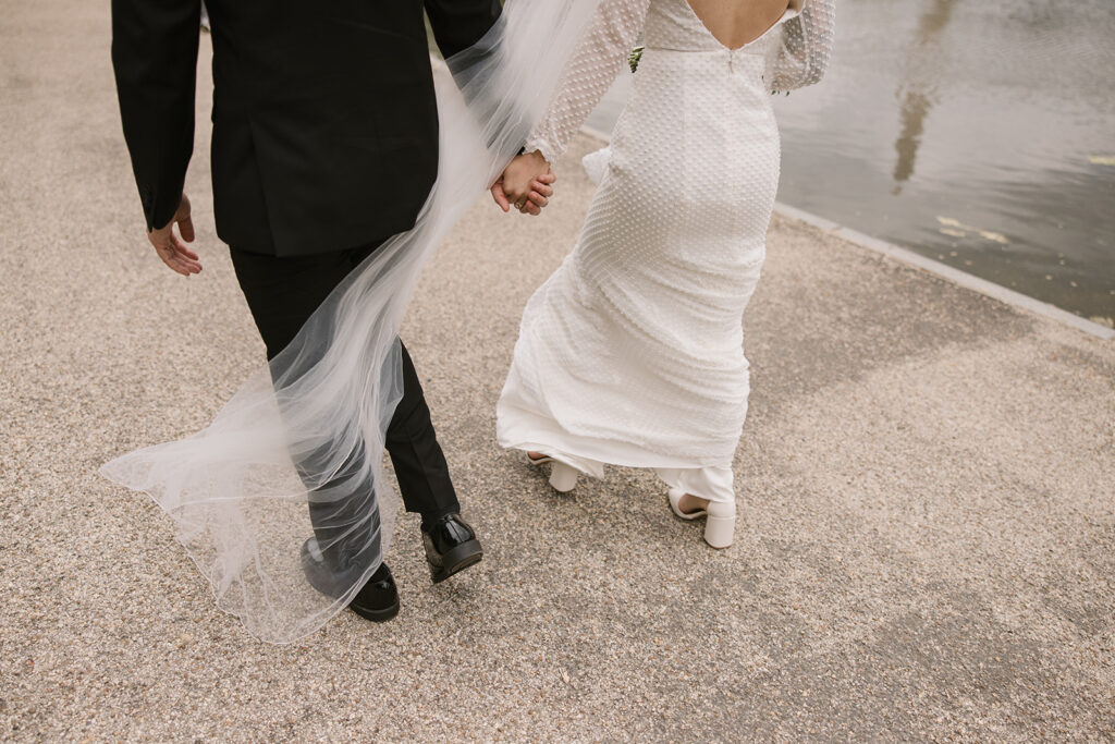 bride and groom holding hands with veil blowing in the wind
