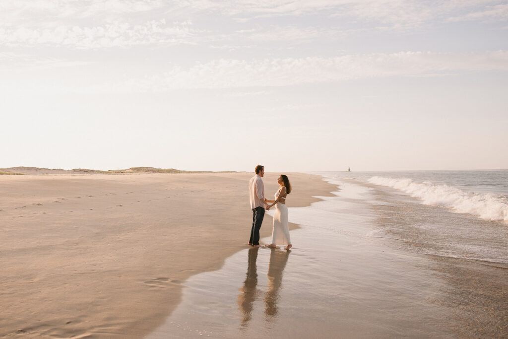 the engaged couple holding hands during their beach engagement session on the east coast