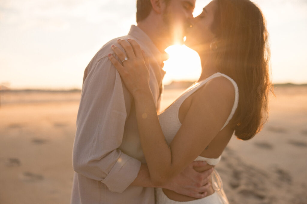 the engaged couple kissing with the sunset behind them during their perfect beach engagement session