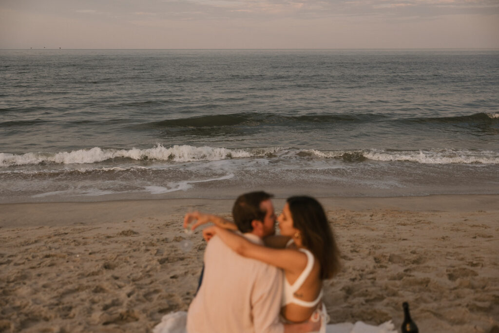 the engaged couple leaning in for a kiss as they sit on their blanket for beach engagement photos