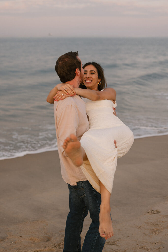 lifting his fiance up to carry her on the beach during their beach engagement photos
