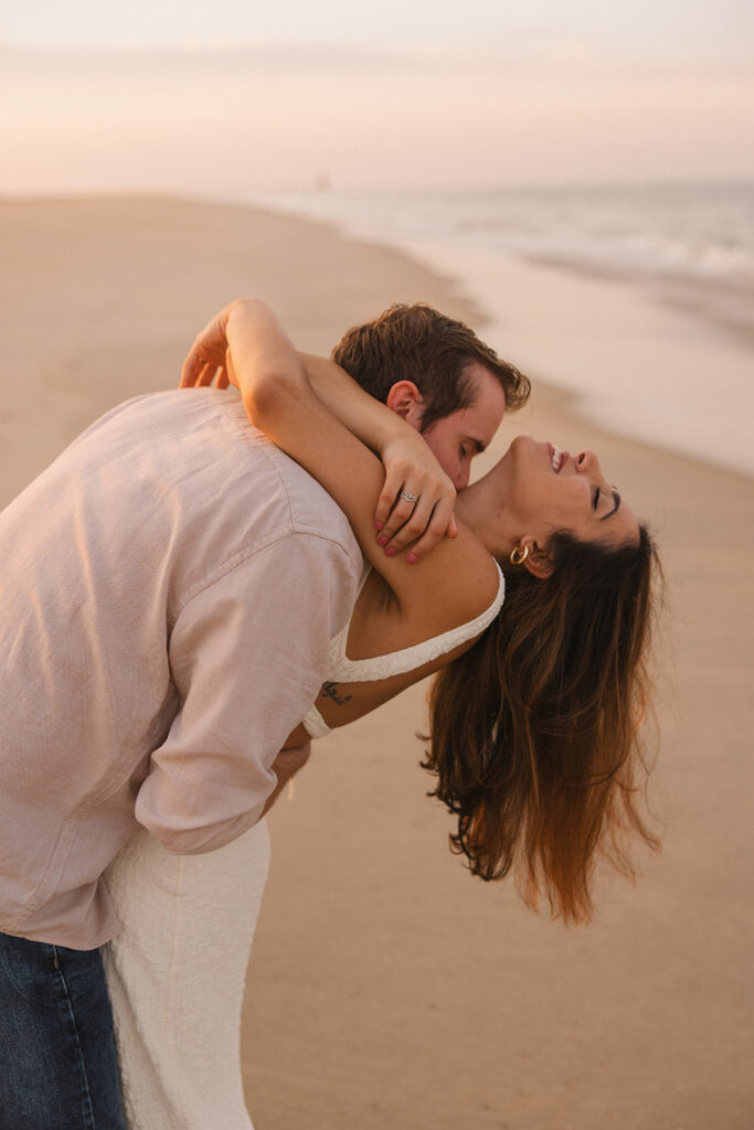 fiance kissing her neck as they laugh during their beach engagement photos