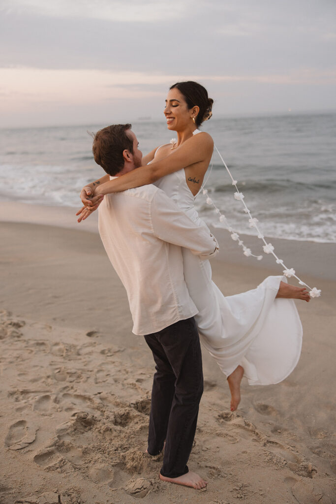 fiance lifting her up for beach engagement photos on the east coast during sunset