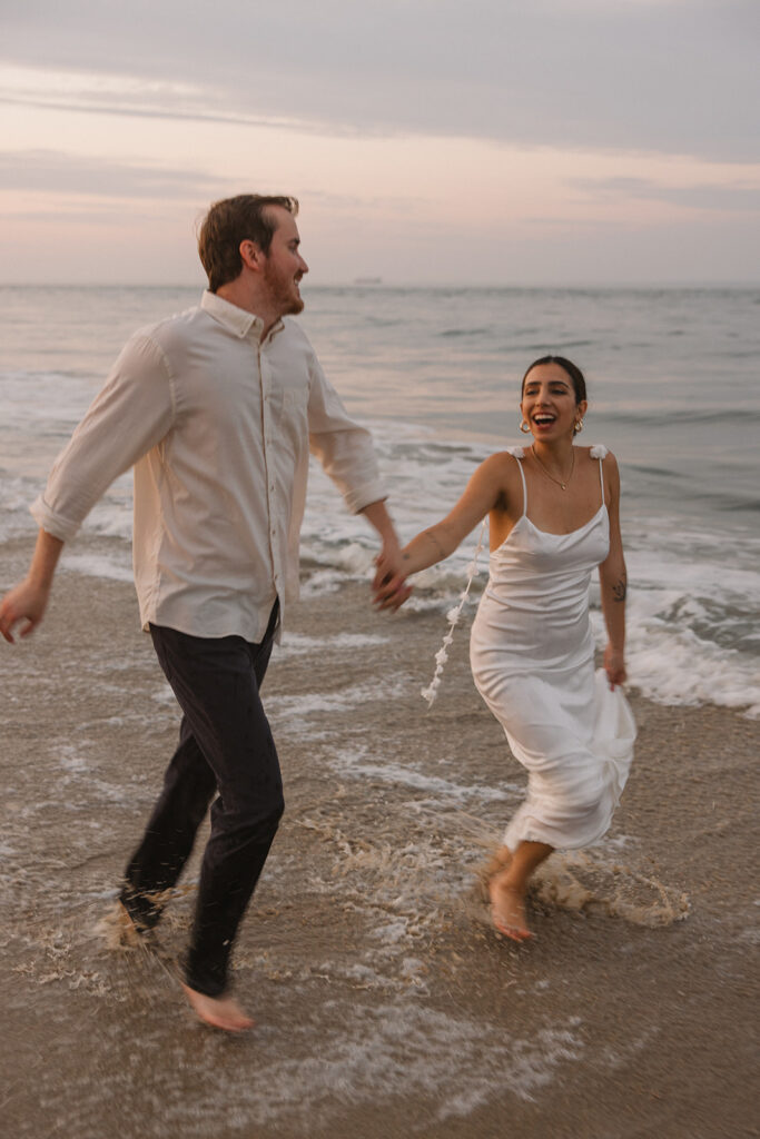 the engaged couple running through the water together during their beach engagement session