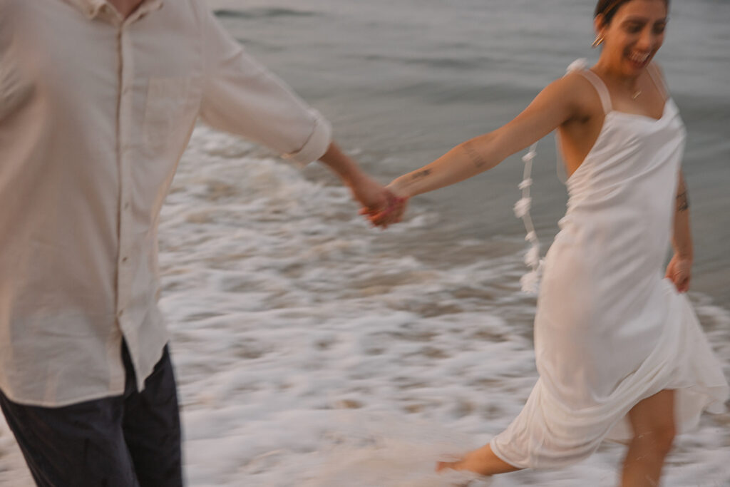 the couple running through the water together for playful beach engagement photos