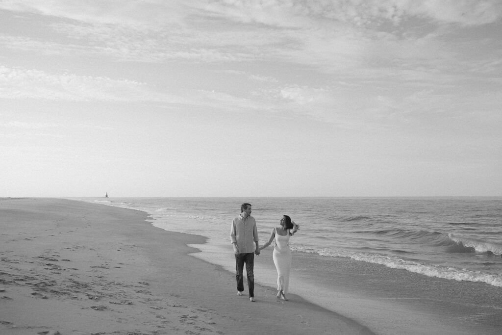 the engaged couple walking along the shore in a black and white beach engagement photo