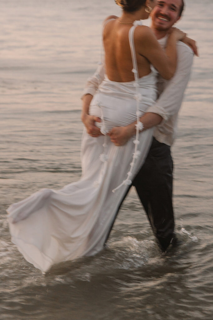 the fiance lifting her up in the waves during their beach engagement photos