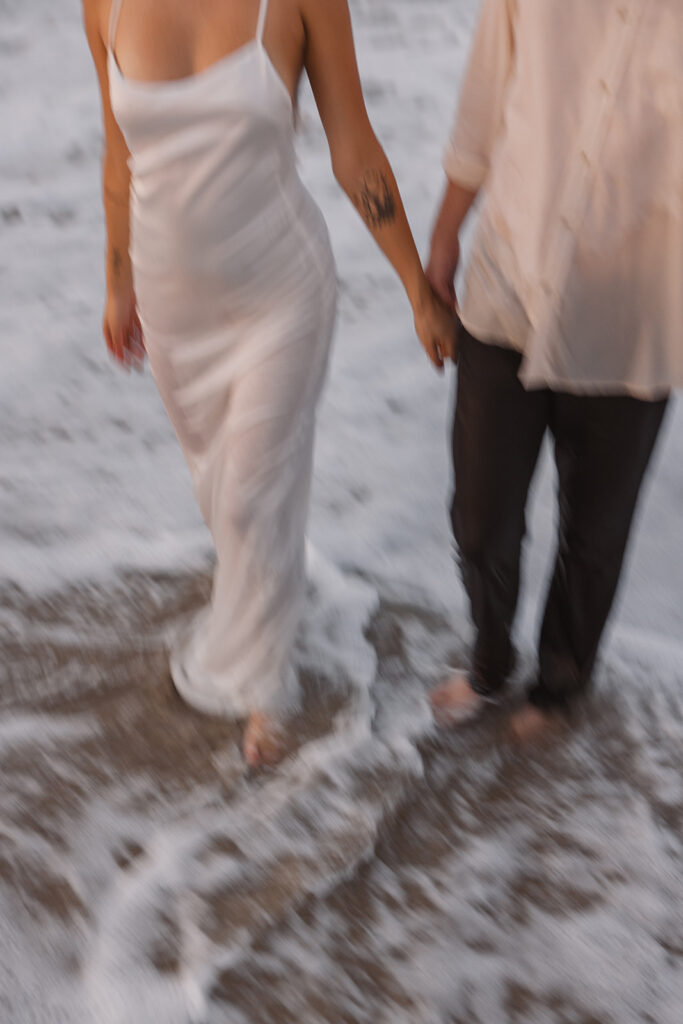 the engaged couple holding hands in the water during their engagement session 