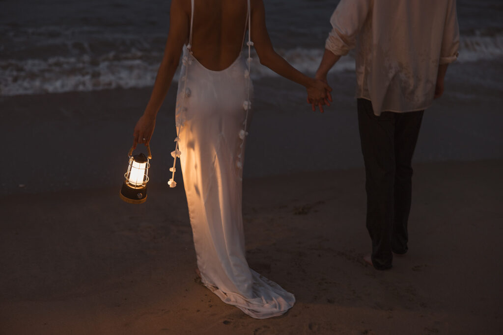 the couple walking on the beach with a lantern as a creative idea for their beach engagement photos