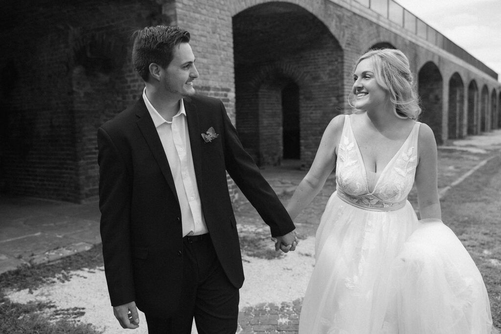 the bride and groom holding hands as they walk in Fort Zachary Taylor State Park