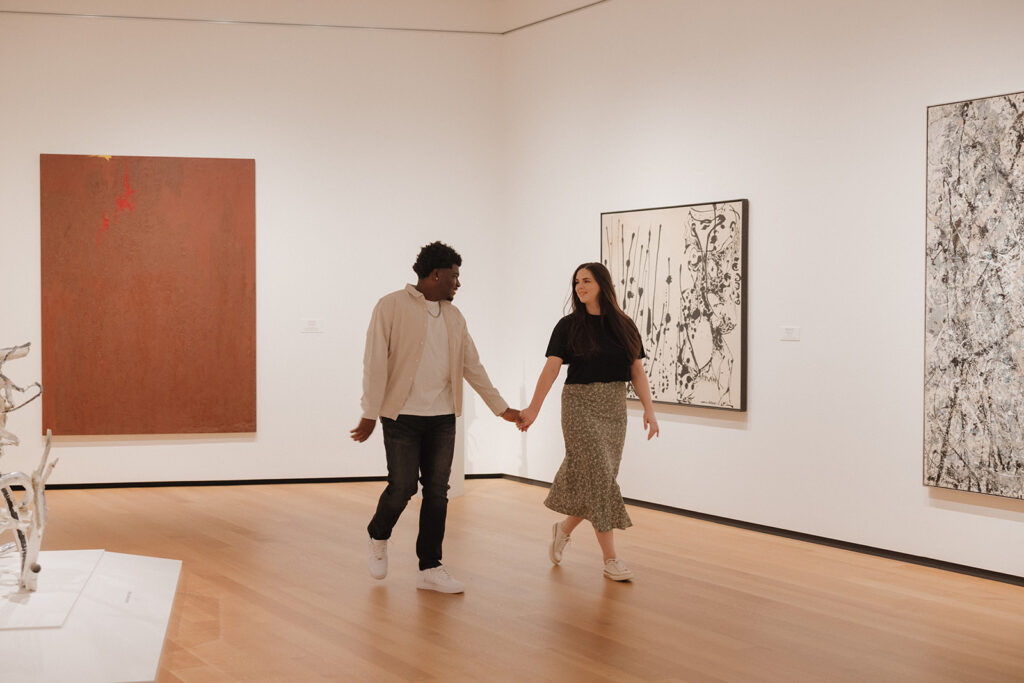 the engaged couple walking through the art gallery as they hold hands