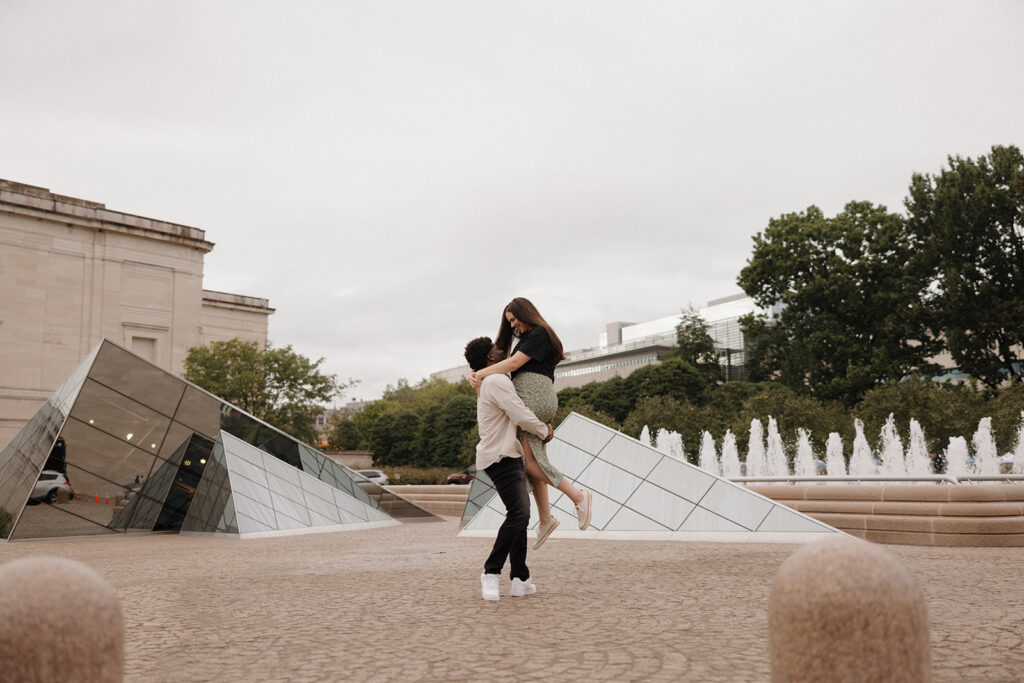 the engaged couple being lifted up outside of the art museum for engagement photos
