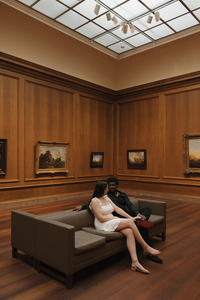 the engaged couple sitting on the bench in the art gallery