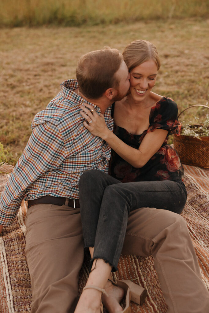 the couple laughing together and kissing her cheek as a part of their proposal story