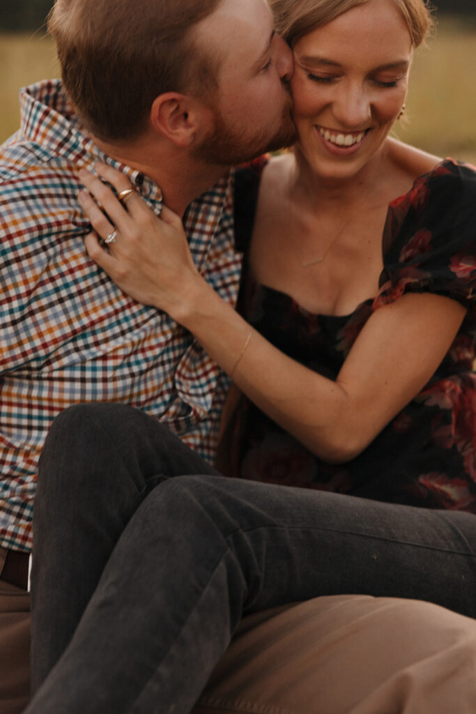 the engaged couple sitting together in the field during their proposal 